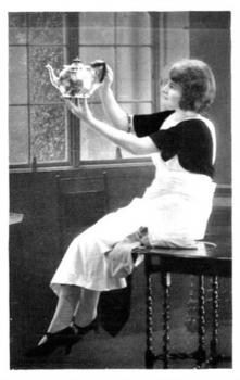 A black and white photo of a young woman holding a silver teapot.